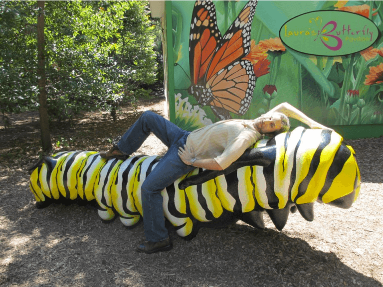 A handsome and charming man laying seductively across a mega sized monarch caterpillar sculpture at the Lincoln Children's Zoo in Nebraska.